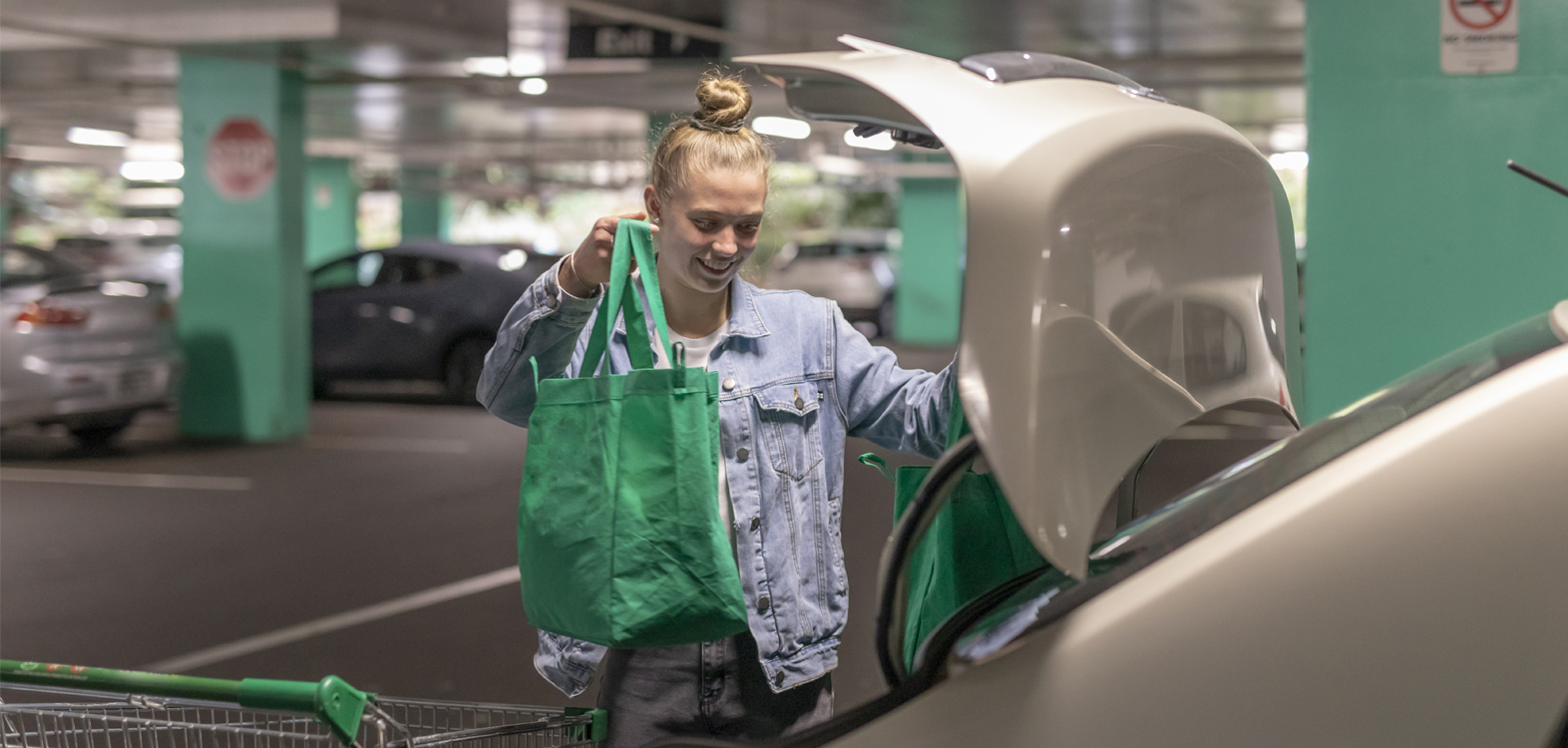 A girl puts shopping in the trunk of a car